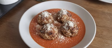 Four air fryer turkey meatballs on marinara sauce with parmesan in a shallow bowl