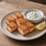 Six baked salmon bites with lemon dill yogurt sauce on a small plate