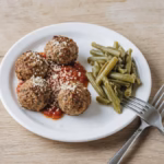 Four small baked lean turkey meatballs with marinara on a small plate