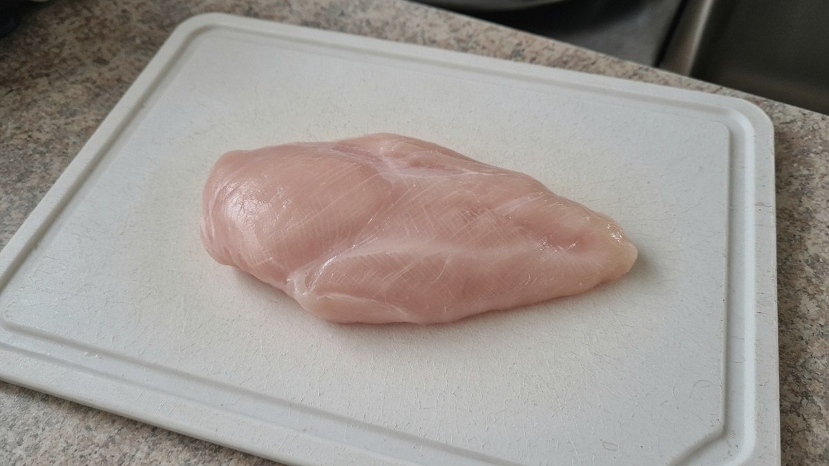 Single raw boneless skinless chicken breast on a cutting board